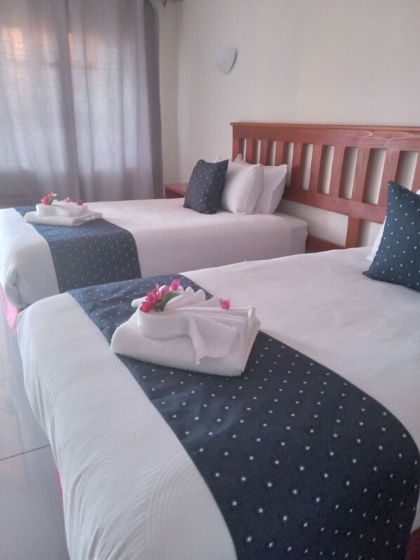 A hotel room with two beds, each with neatly folded white towels and pink flowers.