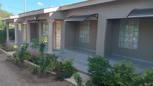 A building with a flat roof, large windows, and a covered entrance with columns. - Rosewood Safari Cottages (Kasane)
