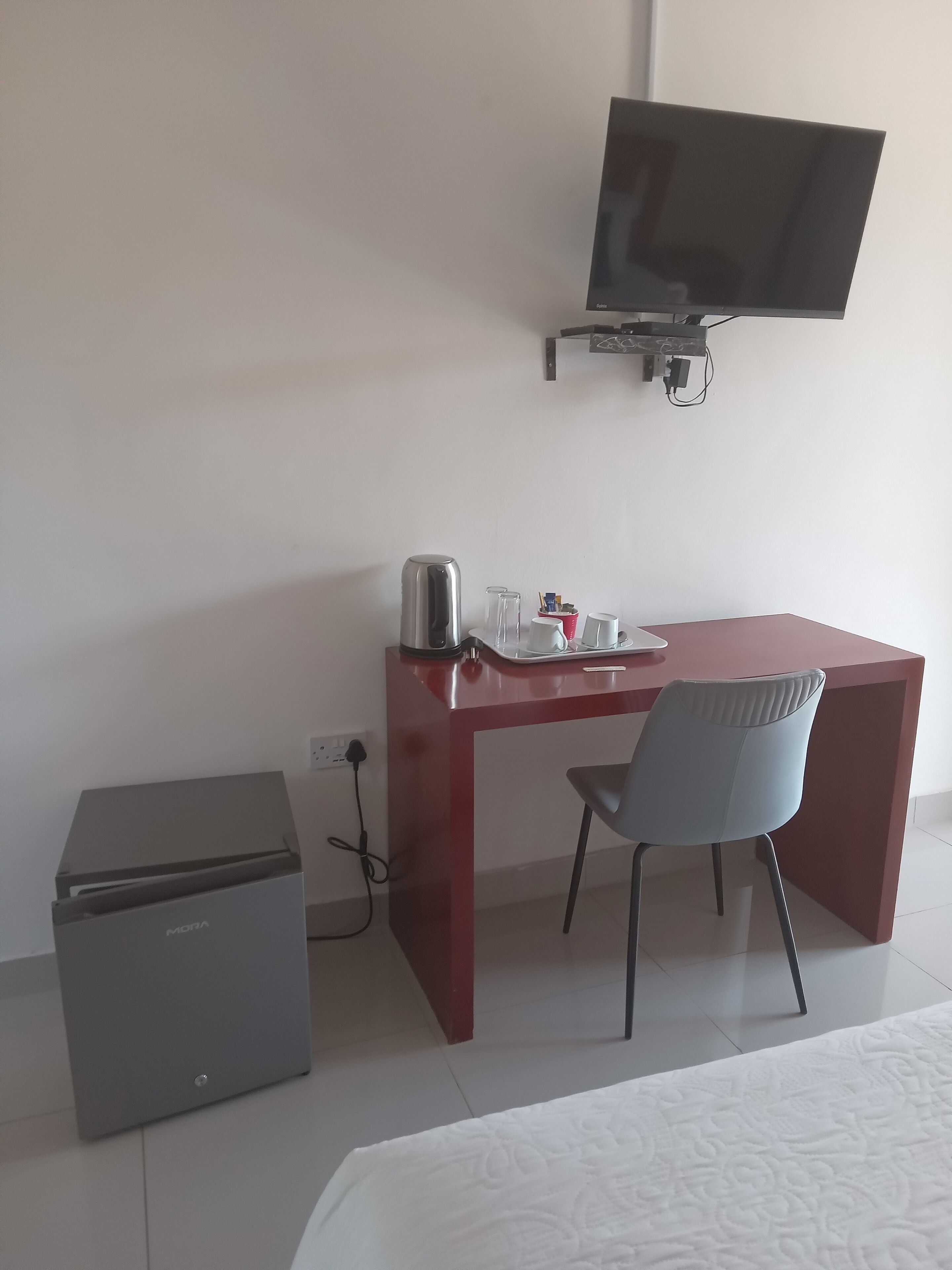 Ein Hotelzimmer mit Schreibtisch, Stuhl, Wandfernseher und kleinem Kühlschrank.
