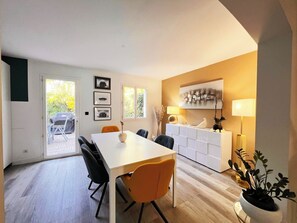 Un espace repas moderne avec une table blanche, des chaises noires et orange, et un meuble blanc sur lequel est posé un objet décoratif.