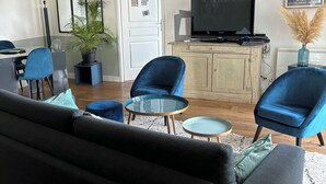 A modern living room with a black sofa, blue armchairs, a glass coffee table, and a television on a wooden cabinet. - Appartement Lumineux à Suresnes à Côté de Paris Vue Tour Eiffel (Suresnes)