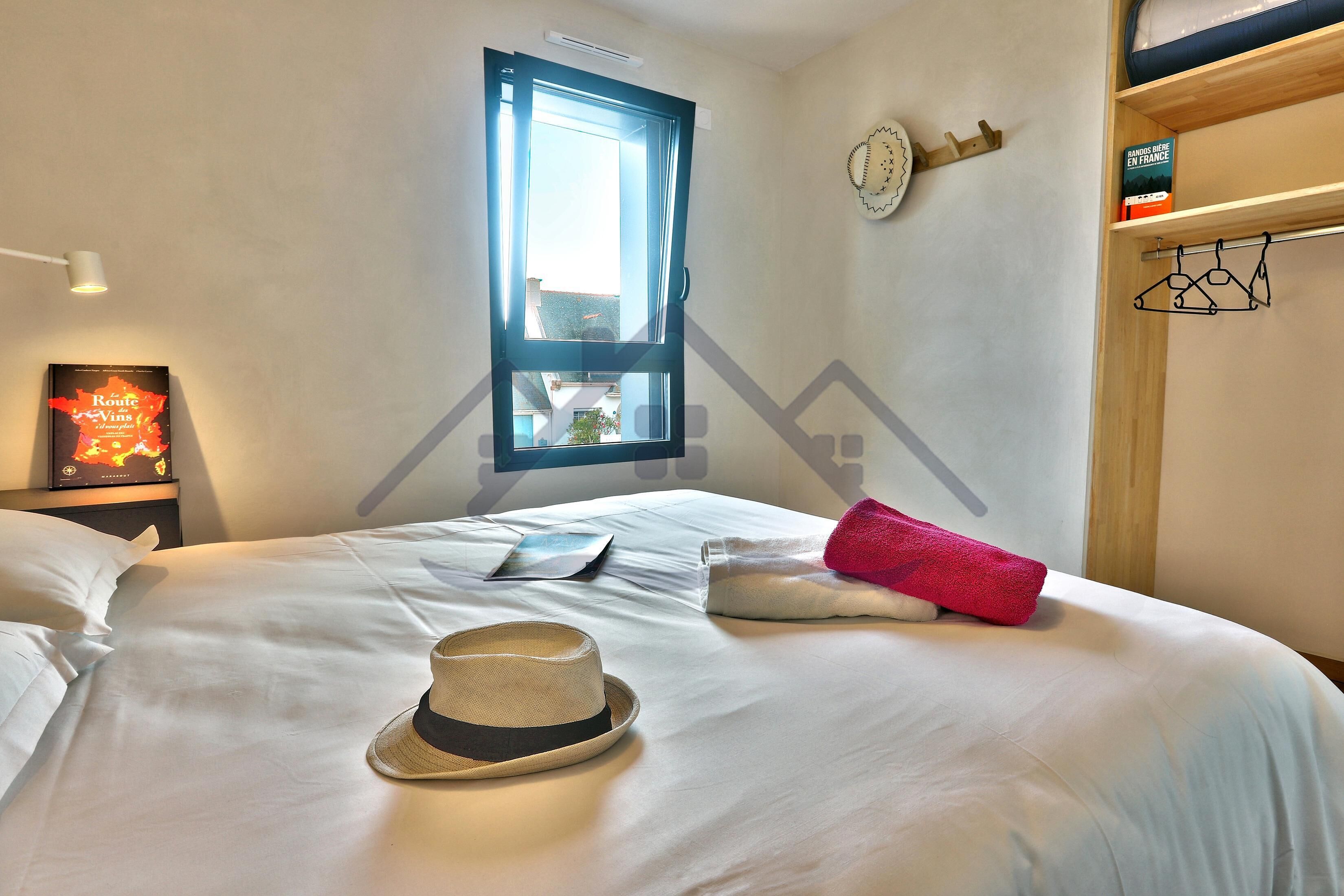 Una cama bien hecha con un sombrero, una almohada y una toalla roja.