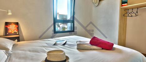 Una cama bien hecha con un sombrero, una almohada y una toalla roja.