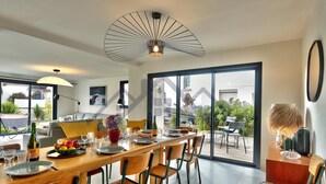 A modern dining area with a wooden table set for four, surrounded by chairs. A large window provides a view of the outdoors. - Large, recently built architect-designed house for 12 people (Guilvinec)