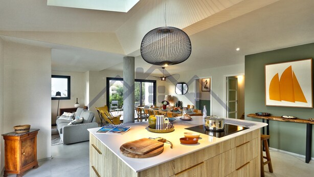 A modern kitchen with a large island, wooden cabinets, and a hanging light fixture. - Large, recently built architect-designed house for 12 people (Guilvinec)