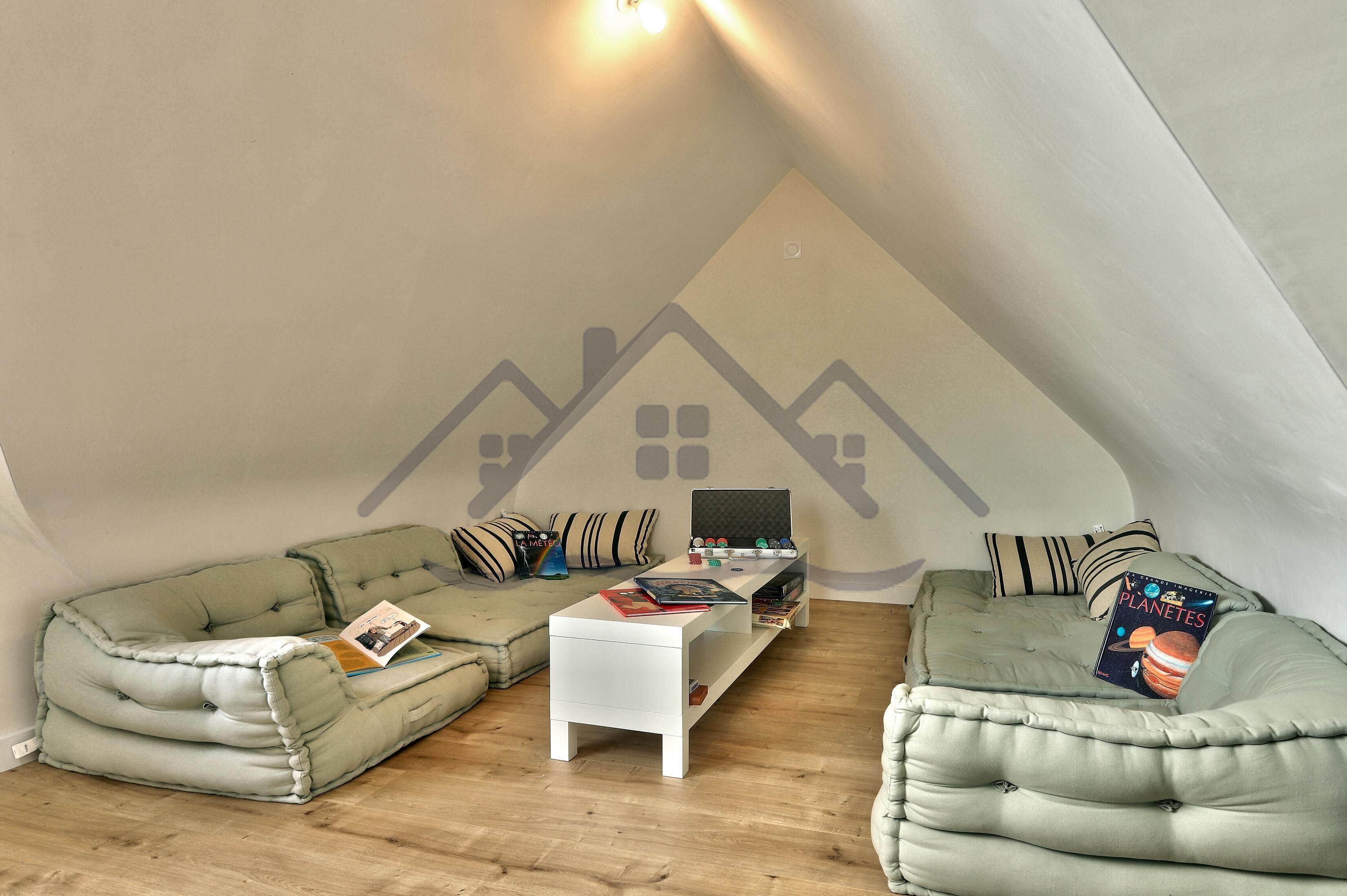 Een gezellig loft slaapkamer met een schuine plafond, een groene bank, een witte salontafel en een boekenkast.