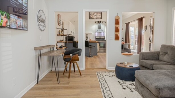 Ett modernt vardagsrum med en grå soffa, ett soffbord i trä och en matplats med ett litet bord och stolar. Man kan se in i köket genom en öppen dörröppning.
