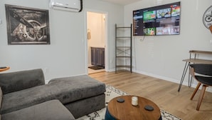 Ett modernt vardagsrum med en grå soffa, ett träbord och en väggmonterad TV som visar olika kanaler.