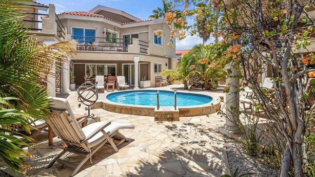 Una casa de dos pisos con piscina, mobiliario exterior y balcón.
