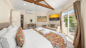 Un dormitorio con cama, escritorio, sofá y balcón con cortinas.