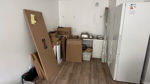 Une petite pièce à aire ouverte comprenant un coin cuisine, un plancher en bois et un réfrigérateur blanc.