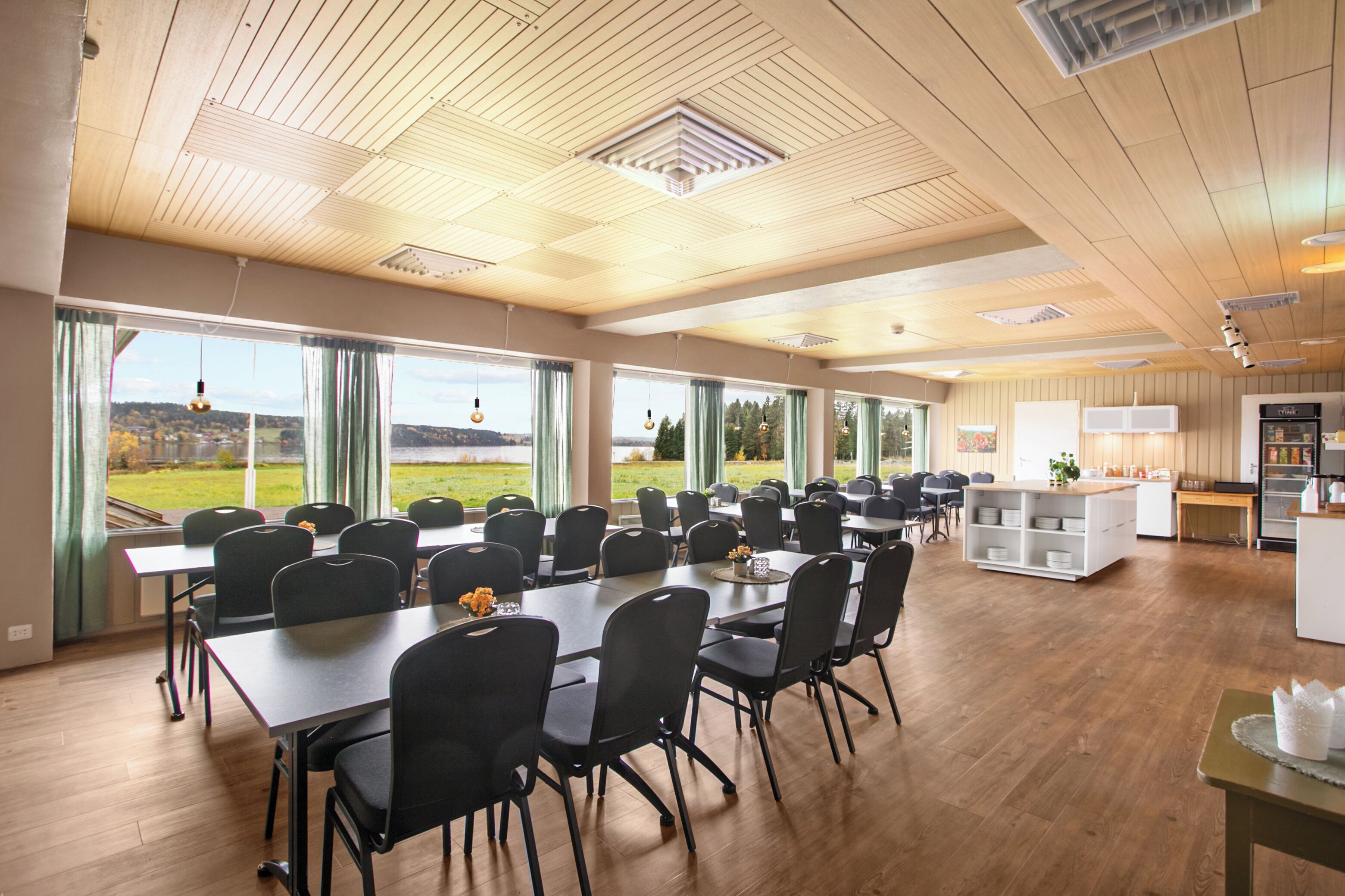Una amplia sala de conferencias con ventanas grandes, una zona de cocina y vistas a un paisaje verde.