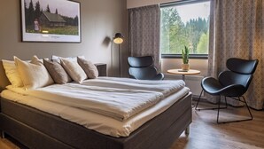 Un dormitorio con una cama grande, dos sillas, una mesita, una lámpara y un ventanal con cortinas.