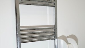 A metal-framed window with horizontal bars, a white chair, and a white wall. - Clean, Spacious 2-bed Apartment in Brierley Hill (Brierley Hill)