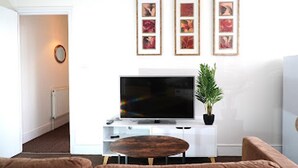 A living room with a flat-screen TV, a potted plant, and a brown sofa. - Clean, Spacious 2-bed Apartment in Brierley Hill (Brierley Hill)