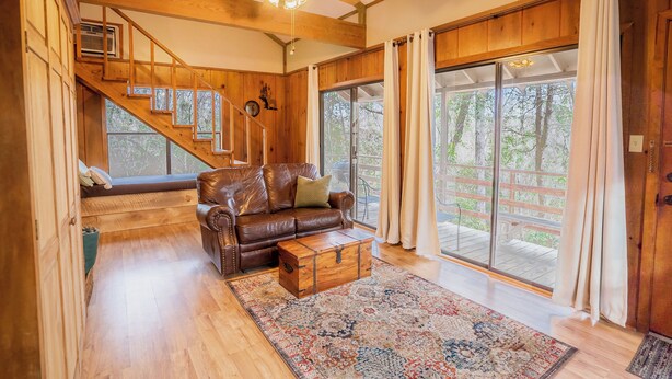 A spacious living room with a wooden staircase, a leather sofa, and a large sliding glass door to the outdoors.