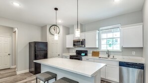 A modern kitchen with white cabinetry, a central island with bar stools, a stainless steel dishwasher, and a microwave above the stove.