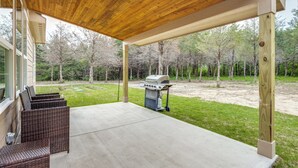 A covered patio with a grill and wicker furniture.