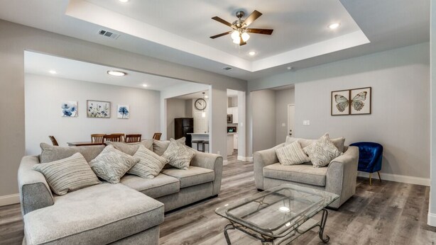 A spacious living room with two grey sofas, a glass coffee table, and a ceiling fan.