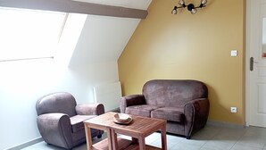 A room with a sloped ceiling, a brown leather sofa, a matching armchair, and a wooden table with a bowl. - Gite Avec Piscine - Périgord Noir - 2 Personnes (Châtres)