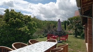 A patio with a table and chairs, surrounded by lush greenery and a view of the sky. - Gite Avec Piscine - Périgord Noir - 2 Personnes (Châtres)