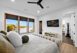 A bedroom with a large bed, a ceiling fan, a stone wall, and a view of a lake. - Lakeside Luxe | Heated Pool | Dock | Sleeps 22 (Hot Springs National Park)