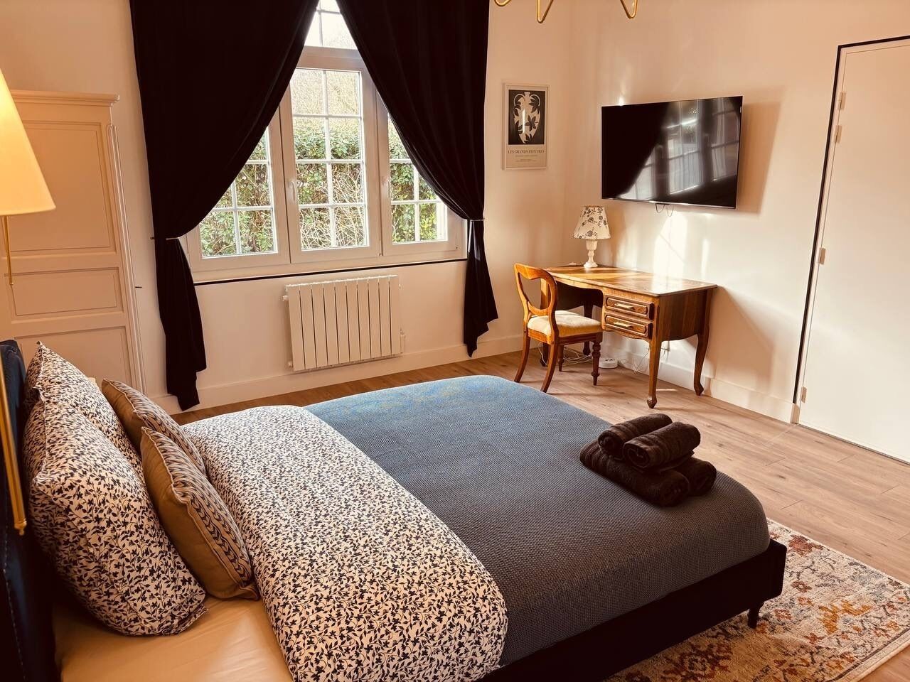 Un dormitorio con una cama, un escritorio, una silla, un televisor y una ventana con cortinas.