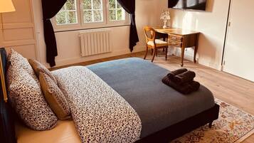 Un dormitorio con una cama, un escritorio, una silla, un televisor y una ventana con cortinas.