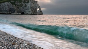 A coastal scene with a rocky beach, waves, and a large cliff formation with a natural arch. - Normandy Etretat (Etretat)