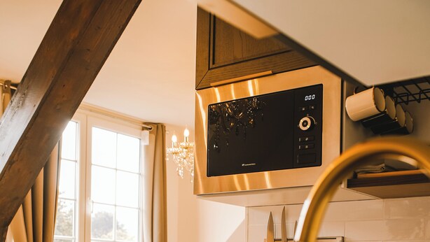 A kitchen with a stainless steel microwave, a sink, and wooden cabinets. - Normandy Etretat (Etretat)