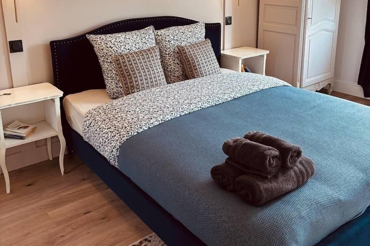 A neatly arranged bedroom with a bed, nightstands, a wardrobe, and patterned wallpaper.