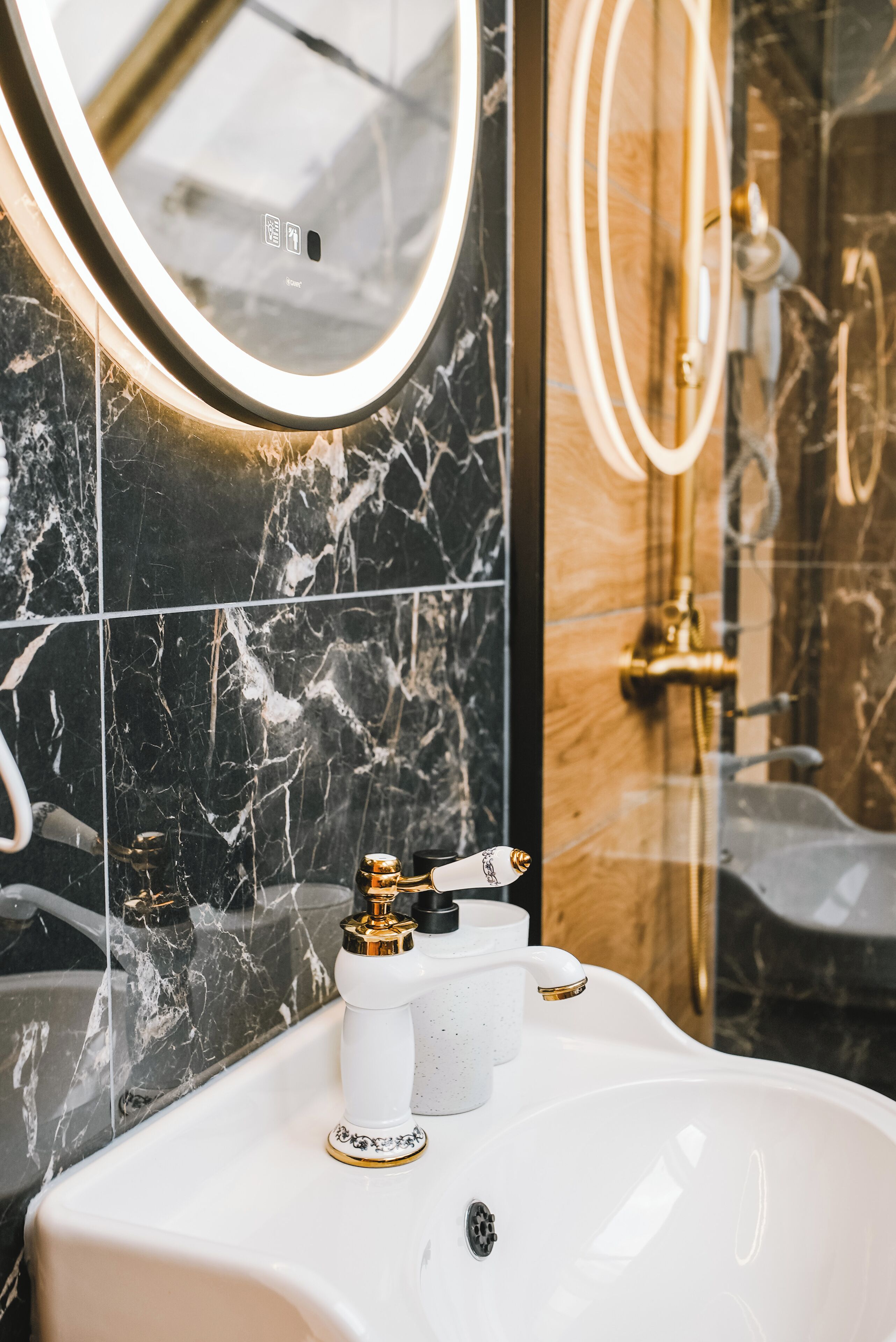 A bathroom with a white sink, gold faucets, and a marble-tiled wall.