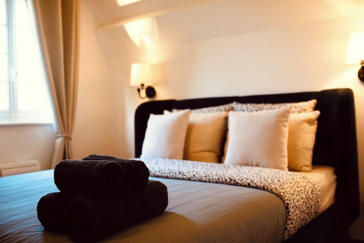 A neatly made bed with a dark brown towel, a patterned throw blanket, and white pillows.