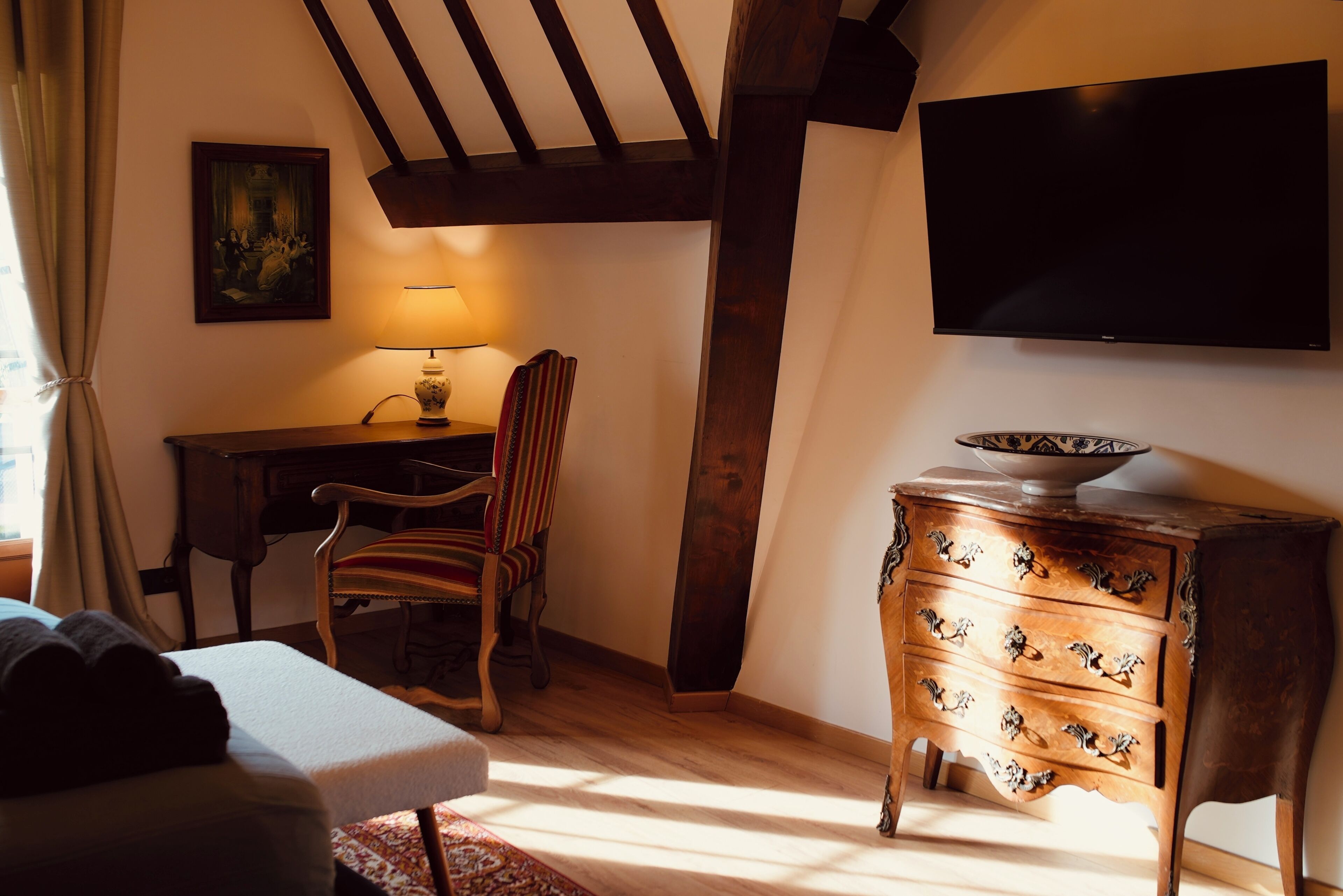 Une pièce confortable avec un bureau en bois, une chaise, une commode à tiroirs et un téléviseur à écran plat fixé au mur.