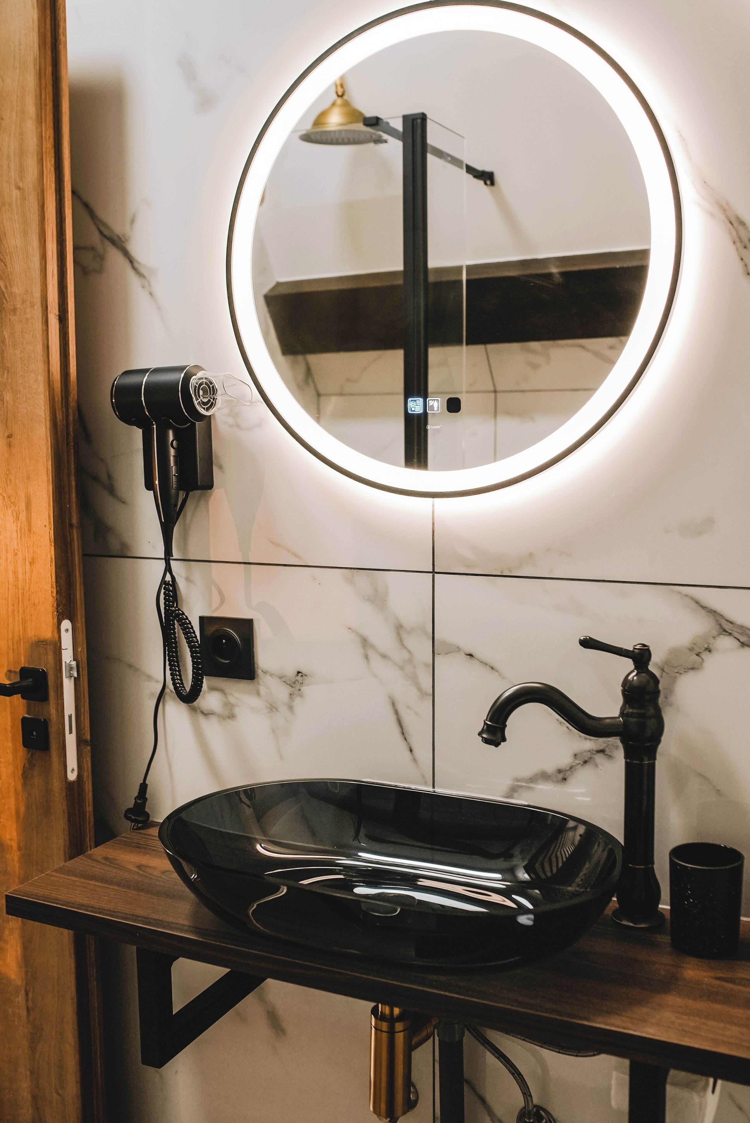 Une salle de bain avec un miroir rond, un lavabo noir et un sèche-cheveux fixé au mur.