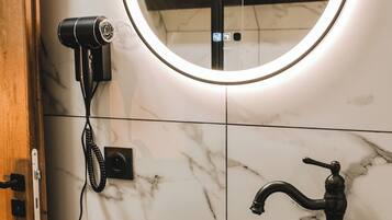 Une salle de bain avec un miroir rond, un lavabo noir et un sèche-cheveux fixé au mur.