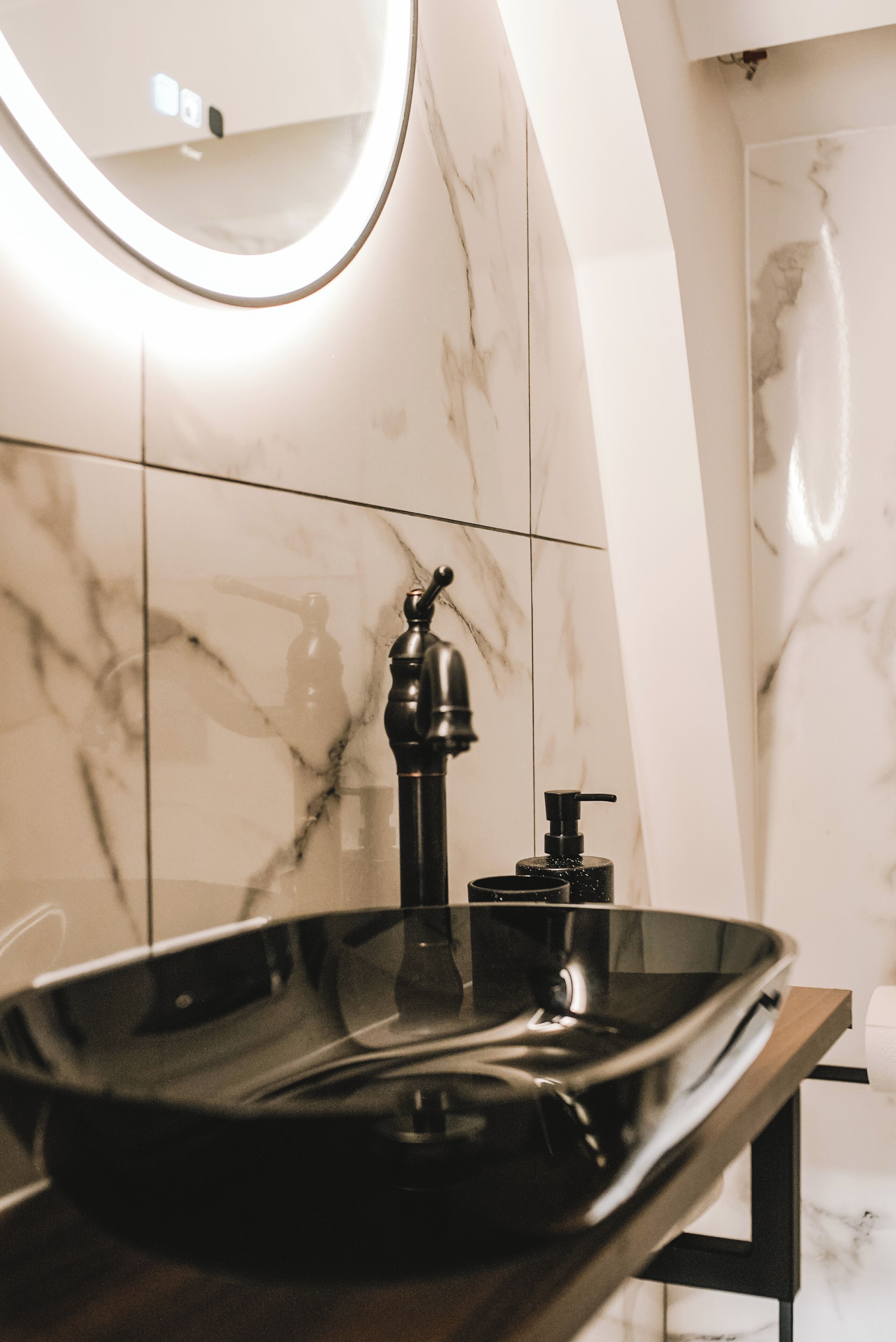 A modern bathroom with a black sink, a round mirror, and marble walls.