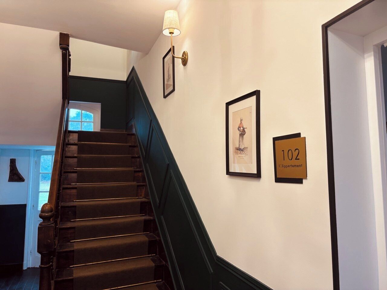 Una escalera con escalones de madera oscura y paredes verdes, que lleva a una puerta con el número 102.
