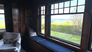 Une pièce chaleureuse avec un banc intégré le long d’une grande fenêtre donnant sur un jardin et la mer.