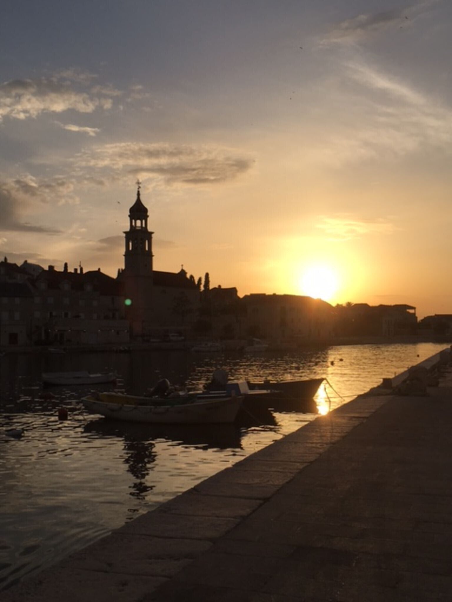 Un coucher de soleil sur une rivière, avec des bateaux et une tour imposante en arrière-plan.