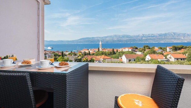 Varanda com mesa posta para café da manhã, com vista para uma cidade costeira com edifícios e uma igreja.