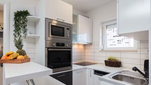 Cozinha moderna com armários brancos, forno embutido, micro-ondas e pia. Há uma janela com vista para o exterior, e uma cesta de frutas no balcão.