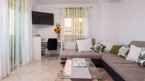 Uma sala de estar moderna com sofá, mesa de centro, televisão e escrivaninha com cadeira.