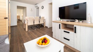 A modern living room with a dining area, a TV, and a fruit bowl on a table. - Two Bedroom Apartment (Lopar)