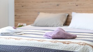 A neatly made bed with a striped bedspread, two pillows, and a folded towel on the bed. - Two Bedroom Apartment (Lopar)