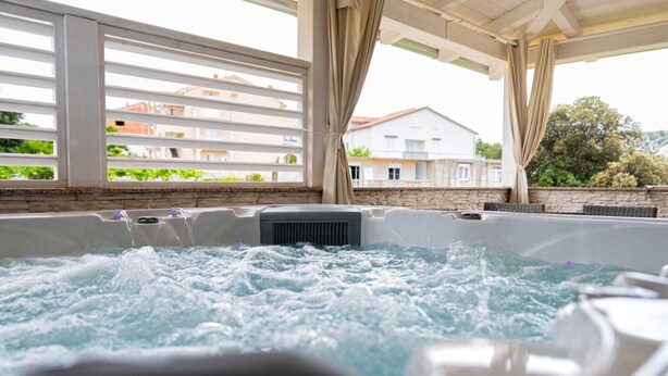 A hot tub area with a view of a building and greenery in the background. - Two Bedroom Apartment (Lopar)