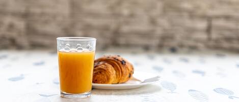 A glass of orange juice and a croissant on a white table with a leaf pattern.