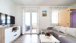 Una sala de estar moderna con un sofá, un televisor, una mesa de centro y un ventanal corredero que da a un espacio al aire libre.
