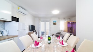 Un comedor moderno con una mesa de madera dispuesta para seis personas, sillas blancas y un televisor al fondo.
