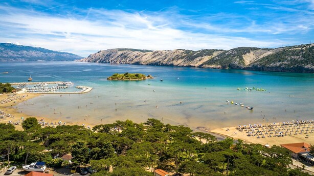 Escena costera con playa de arena, cielos despejados y una pequeña isla.